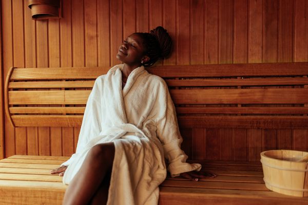 mulher negra sentada em uma sauna com um sorriso no rosto e olhos fechados