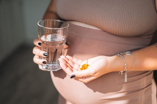 jovem grávida com um copo de água e suplementos dietéticos nas mãos