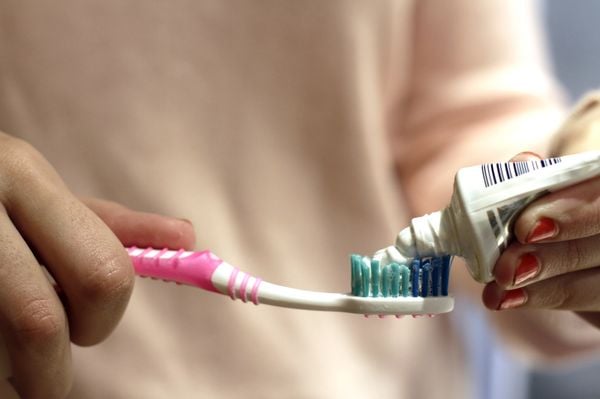 Mãos femininas segurando escova de dente enquanto coloca pasta dental