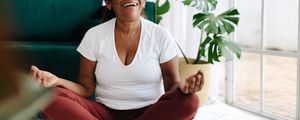 Mulher feliz meditando na posição de lótus em casa