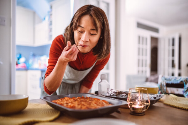 Mulher inclinada em mesa com garfo na boca comendo sobremesa que está em cima da mesa