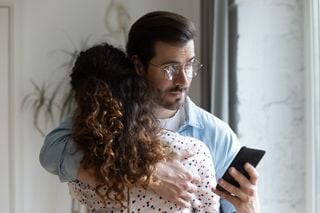 Homem olhando o celular enquanto abraça a esposa