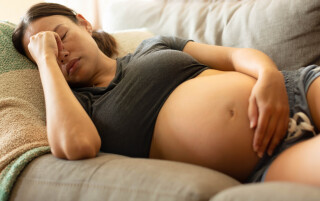 Mulher grávida deitada de lado em sofá com uma mão na barriga e um no rosto