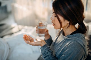Mulher tomando comprimido com um copo de água na mão