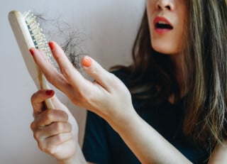 Close de uma mulher segurando uma escova de cabelos, onde estão vários fios de cabelo