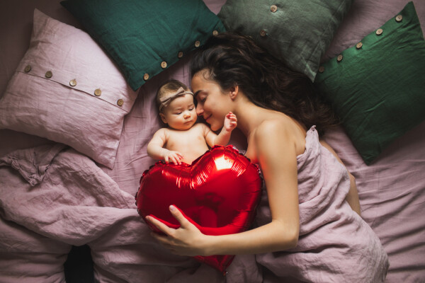 mãe e seu bebê deitadas na cama segurando um balão em formato de coração