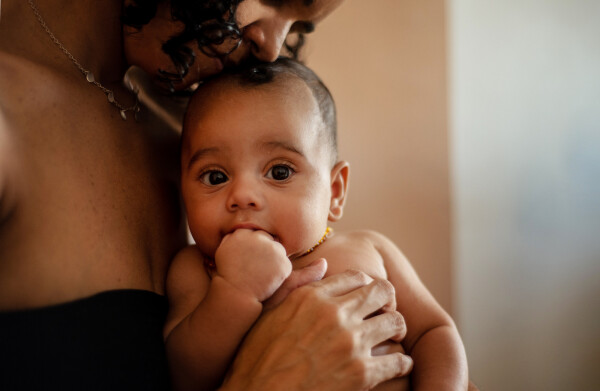 Bebê no colo da mãe com o dedo na boca