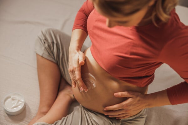 Visão de cima de uma mulher grávida passando creme na barriga