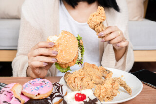 Mulher comendo hambúrguer, frango e donuts sentada em uma mesa