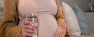 Mulher grávida sentada com um comprimido de remédio na mão