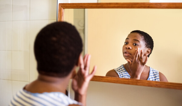 Mulher passando creme no rosto em frente ao espelho