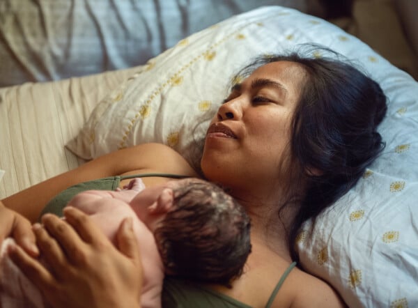 Mulher segurando um bebê recém-nascido na cama de sua casa, após parto domiciliar