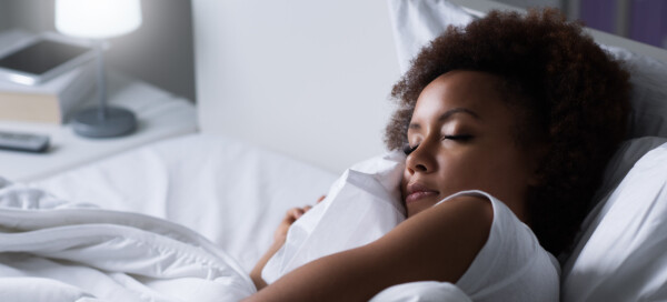 Mulher negra dormindo em uma cama de lençois brancos