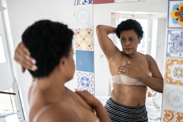 Mulher de meia idade em frente ao espelho observando as mamas