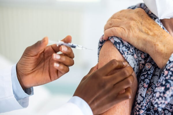 Foto aproximada de enfermeira aplicando vacina no braço de uma senhora