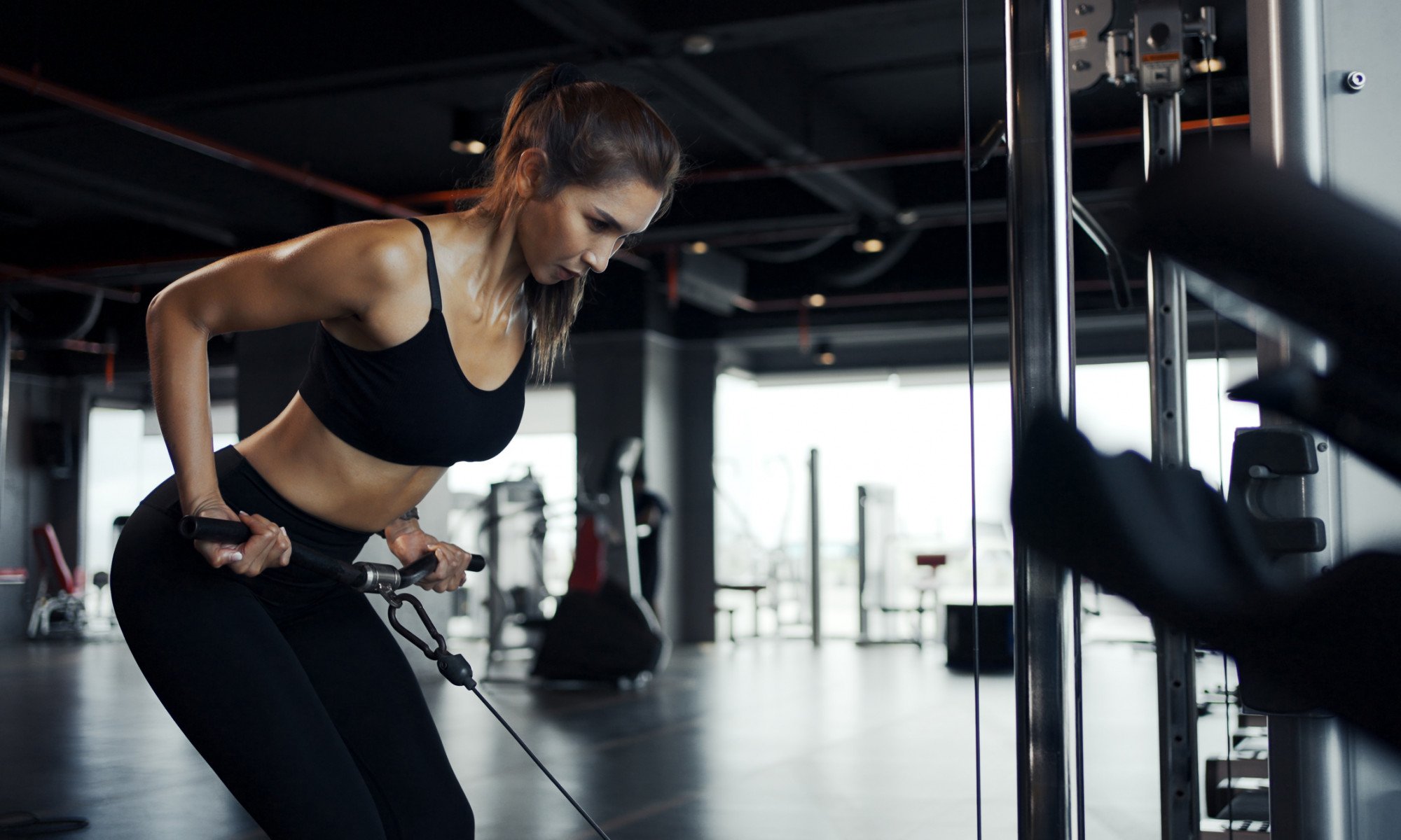 Mulher jovem em forma fazendo exercício em máquina de crossover na academia