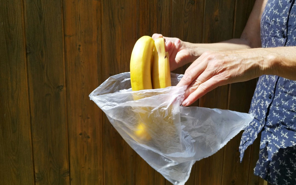 Mãos femininas colocando bananas em um saco plástico