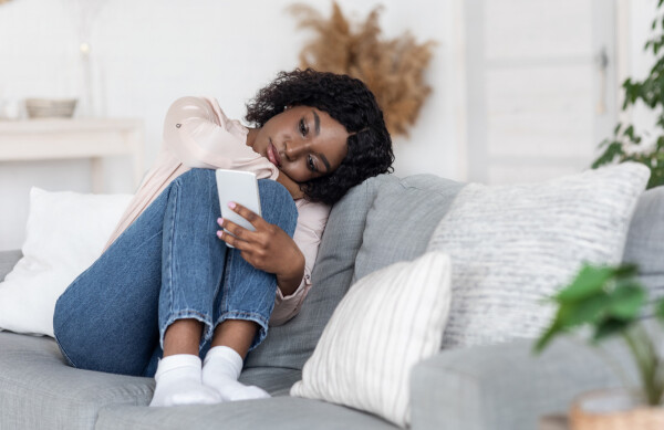 Mulher sentada no sofá, com as pernas dobradas, segurando o celular