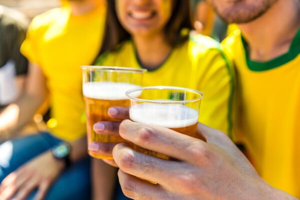 Homem e mulher usando camiseta amarela da seleção brasileira segurando copo com cerveja