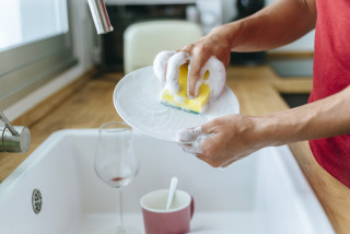 Imagem aproximada de homem lavando louça com esponja