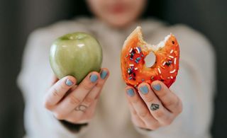 Mulher desfocada com uma maçã e um donut nas mãos
