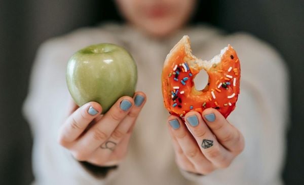 Mulher desfocada com uma maçã e um donut nas mãos