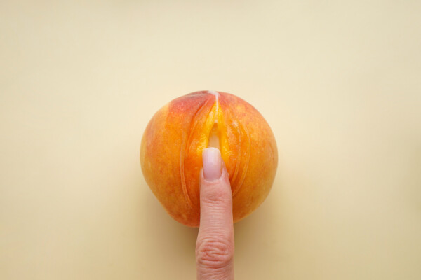 imagem de um dedo tocando um pêssego aberto, representando o clitóris