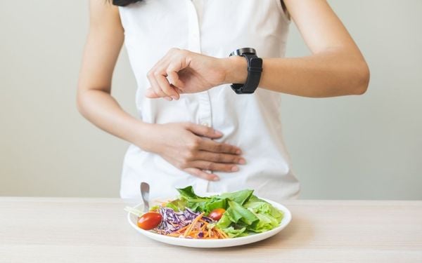 foto de mulher com mão na barriga em frente a um prato de salada