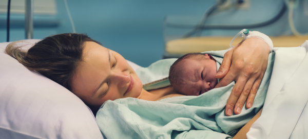 Mulher deitada em cama do hospital após o parto segurando o bebê recém-nascido no colo