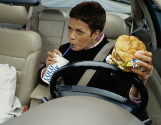 Mulher comendo hambúrguer e dirigindo  