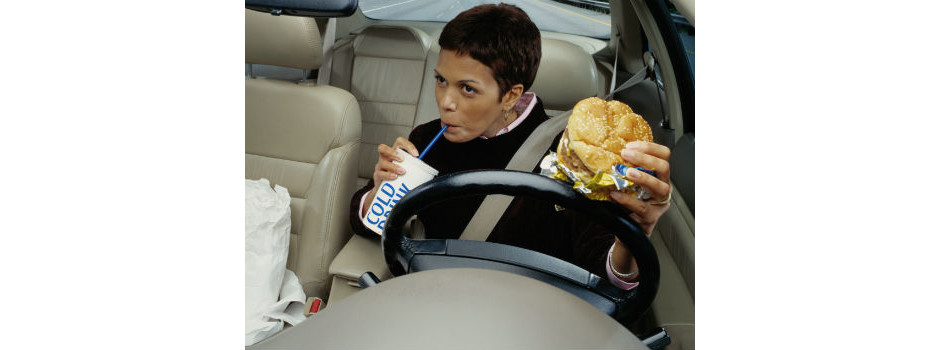 Mulher comendo hambúrguer e dirigindo  
