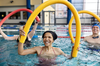 Mulher idosa fazendo exercícios de hidroginástica na piscina com a ajuda de um assessório