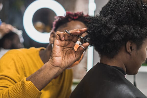 cabelereiro em salão cortando cabelo crespo de cliente com uma tesoura