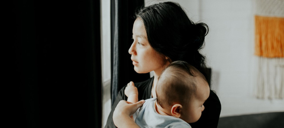 Mãe segura seu bebê no colo enquanto olha pela janela