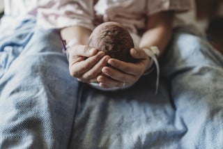 Mãe segurando recém-nascido em cama de hospital