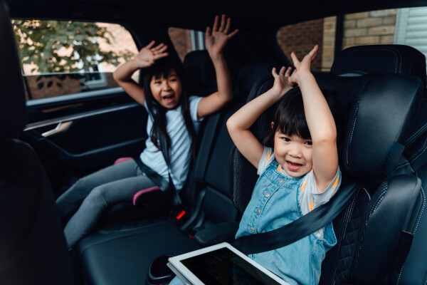 Duas crianças sentadas no banco de trás do carro com as mãos levantadas