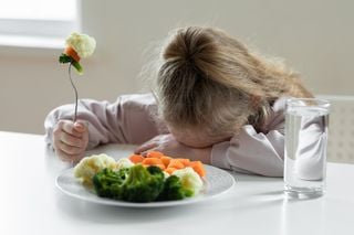 Menina com a cabeça abaixada, se recusando a comer vegetais cozidos