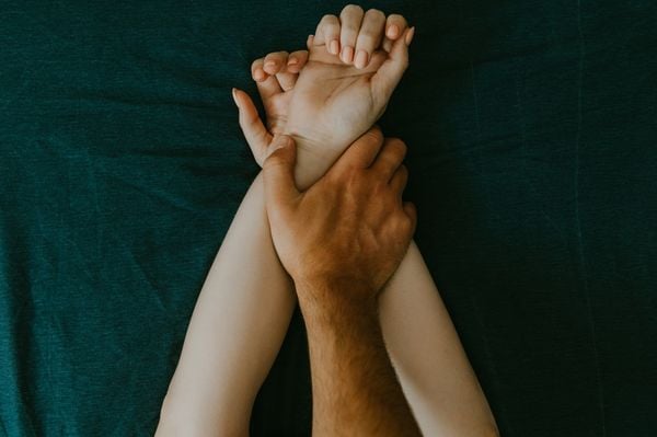 mão masculina segurando braços femininos sobre a cama