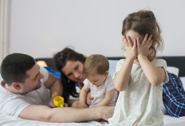 Criança chorando enquanto os pais brincam com um bebê ao fundo