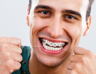 Homem com aparelho ortodôntico passando fio dental