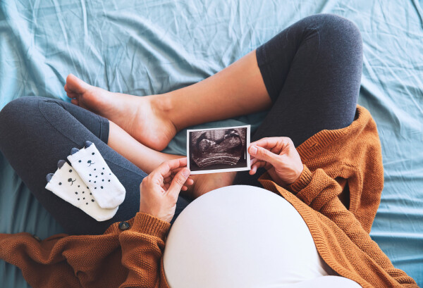 Mulher grávida com barriga em evidência segurando foto de ultrassom do bebê
