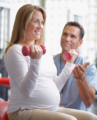 grávida levantando dois halteres com a orientação de um personal - Foto Getty Images