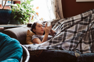 Adolescente deitada no sofá enquanto mexe no celular