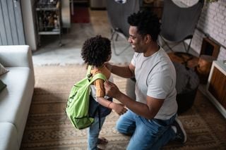 Pai agachado enquanto arruma a mochila do filho pequeno