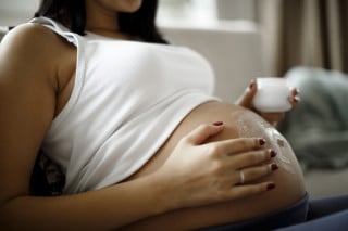 Mulher grávida passando hidratante na barriga