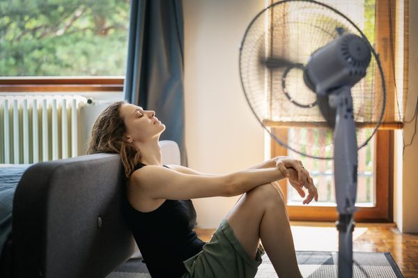 mulher sofrendo com o calor sentada no chão de casa na frente de um ventilador