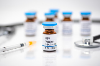 Frasco de vacina para o Vírus Sincicial Respiratório (VSR); ao fundo, seringas e mais frascos