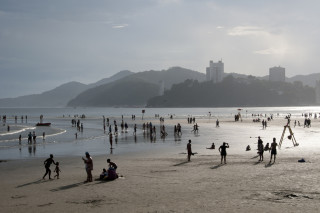 Pessoas na areia e tomando banho de mar em praia de Santos, São Paulo