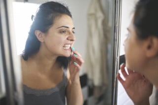 Mulher analisando os próprios dentes em frente ao espelho