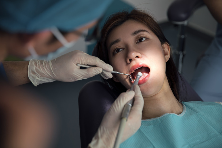 mulher asiática com a boca aberta em mesa de dentista fazendo procedimento dentário